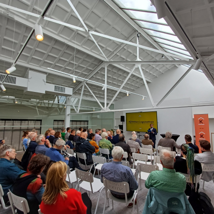 Foto mensen in theateropstelling die naar een presentatie kijken in een witte lichte zaal.