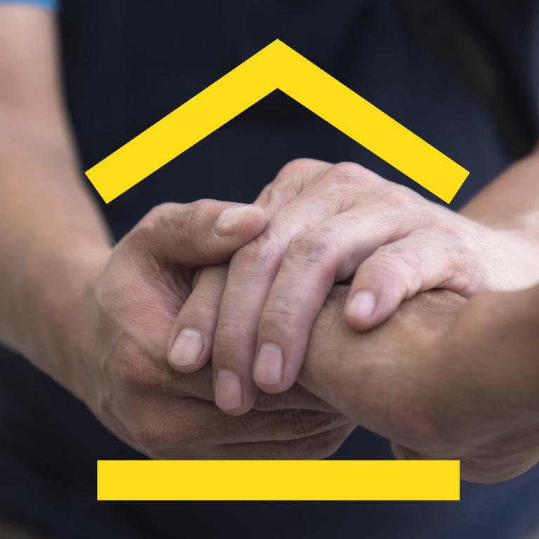 De afbeelding toont een persoon die de hand van een ander persoon op een steunende en zorgzame manier vastpakt met beide handen.