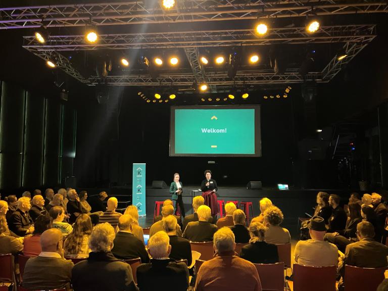 Financiering café in de zaal van ECI Cultuurfabriek. Mensen in theateropstelling en presentatoren.