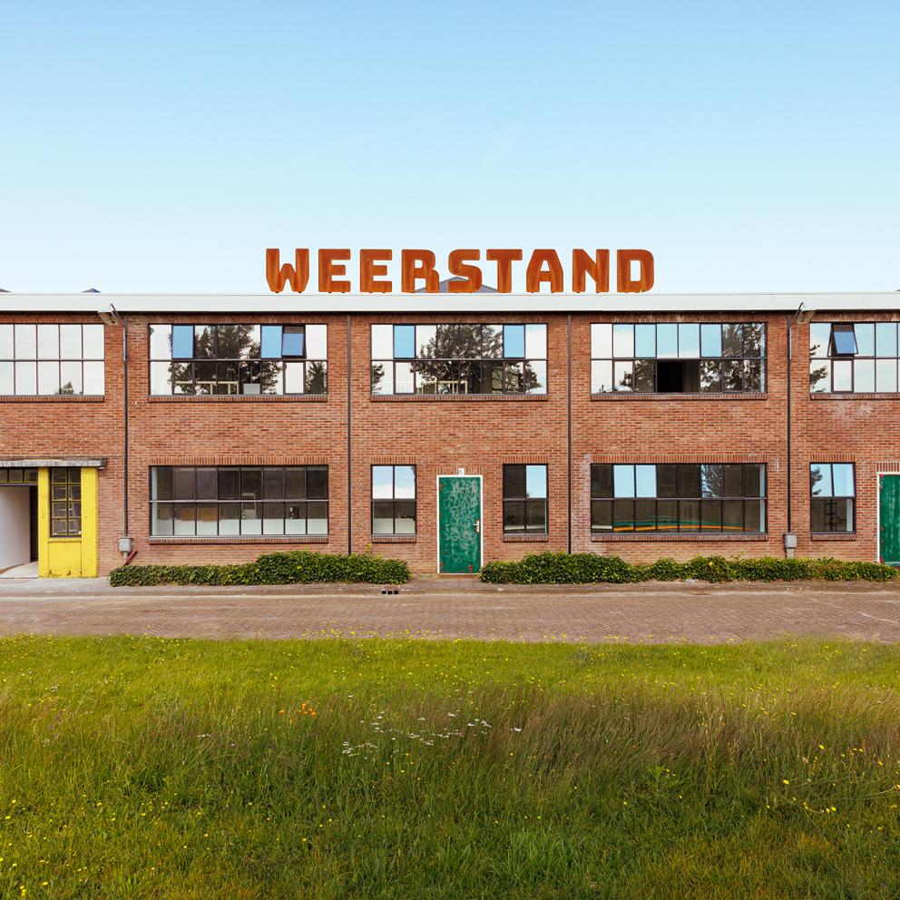 Gevel Weerstand, Logo Huis voor de Kunsten Limburg, Blauwe lucht, Wolken, Gras.