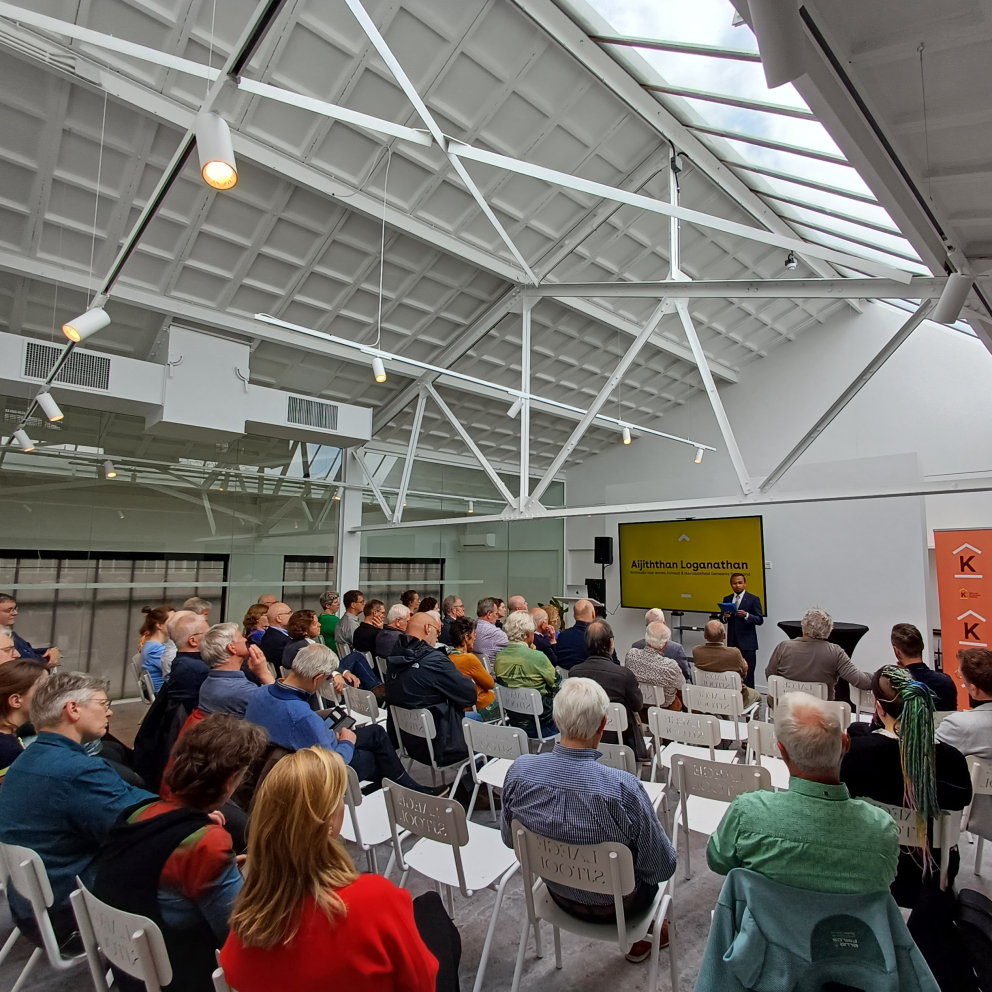 Foto mensen in theateropstelling die naar een presentatie kijken in een witte lichte zaal.