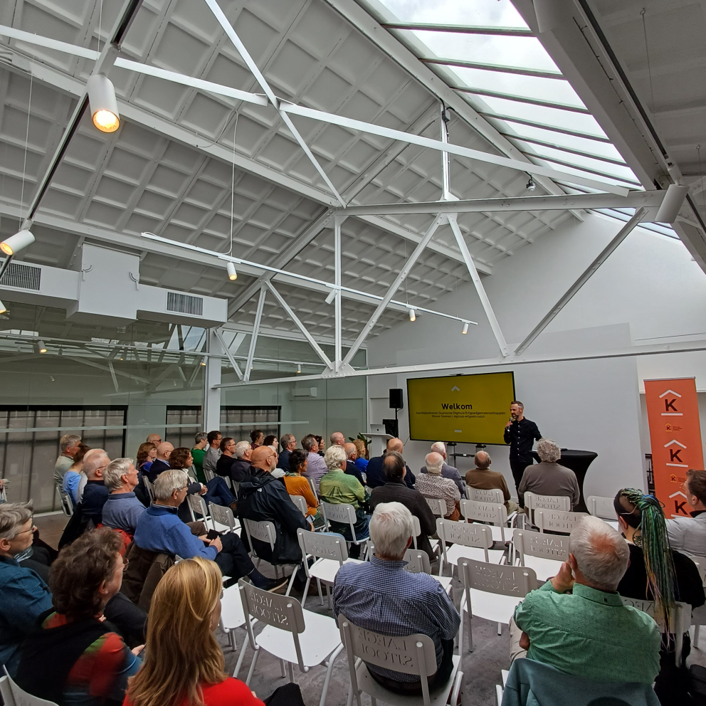 Foto van mensen in theateropstelling die naar een presentatie kijken tijdens de startbijeeenkomst van het Faro project van AEZEL in een witte lichte zaal.