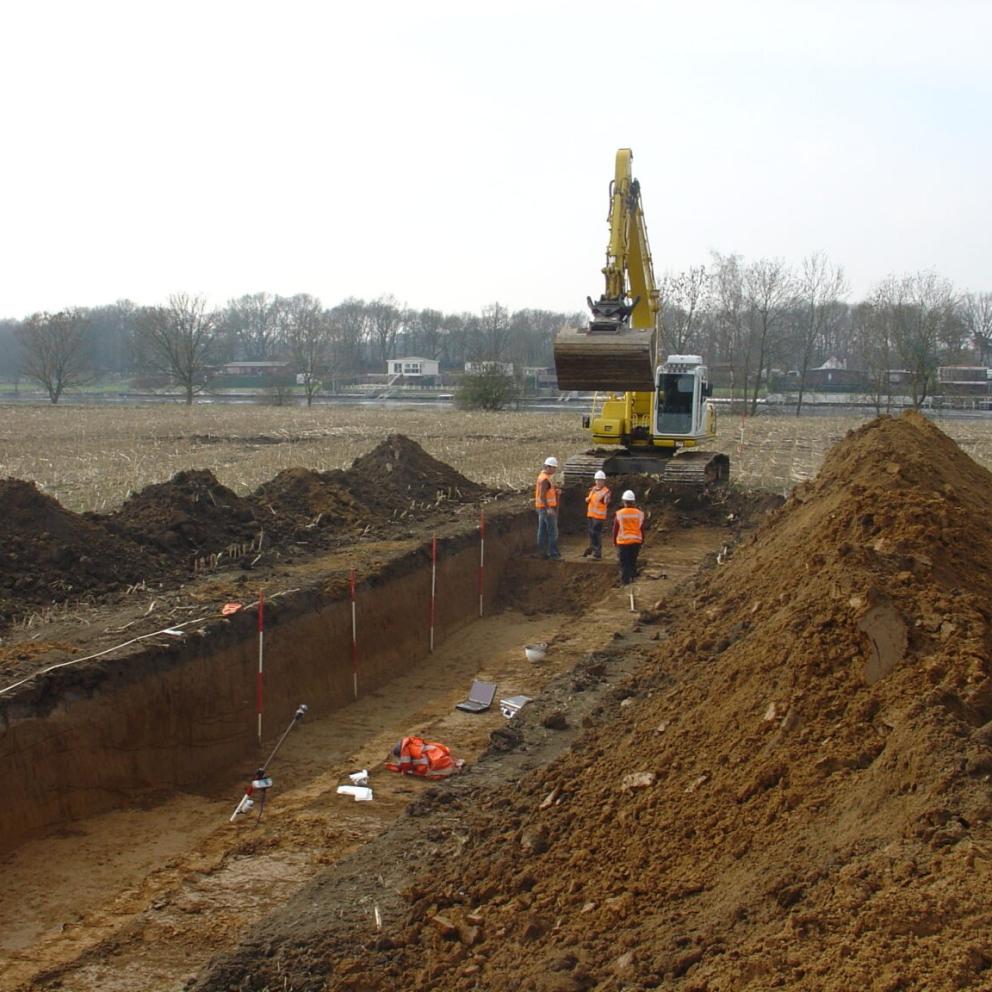 Archeologen leggen met behulp van een graafmachine proefsleuven aan in een veld.