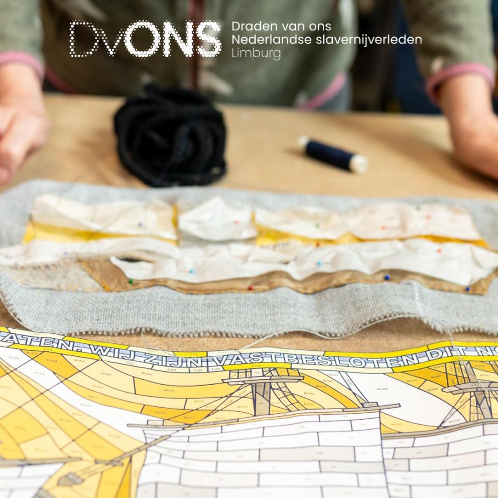 Een persoon die aan een tafel staat met daarop een textielwerk. Op de afbeelding staat de tekst: ‘Draden van ons Nederlandse slavernijverleden Limburg.